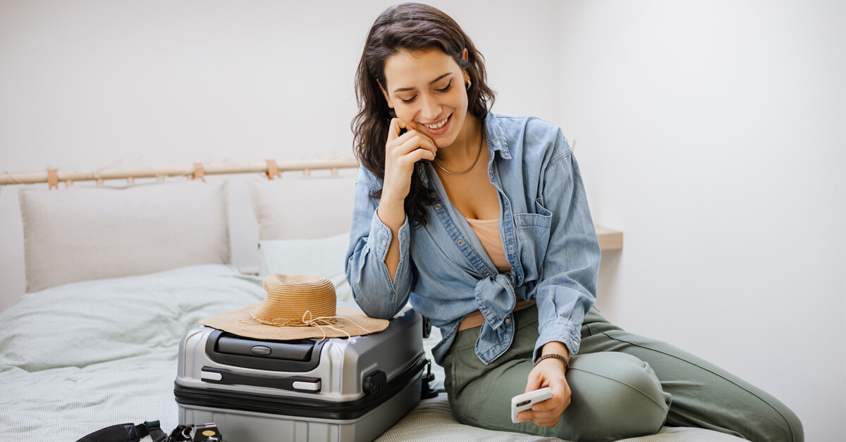 woman sitting on bed with luggage looking at phone Thumbnail