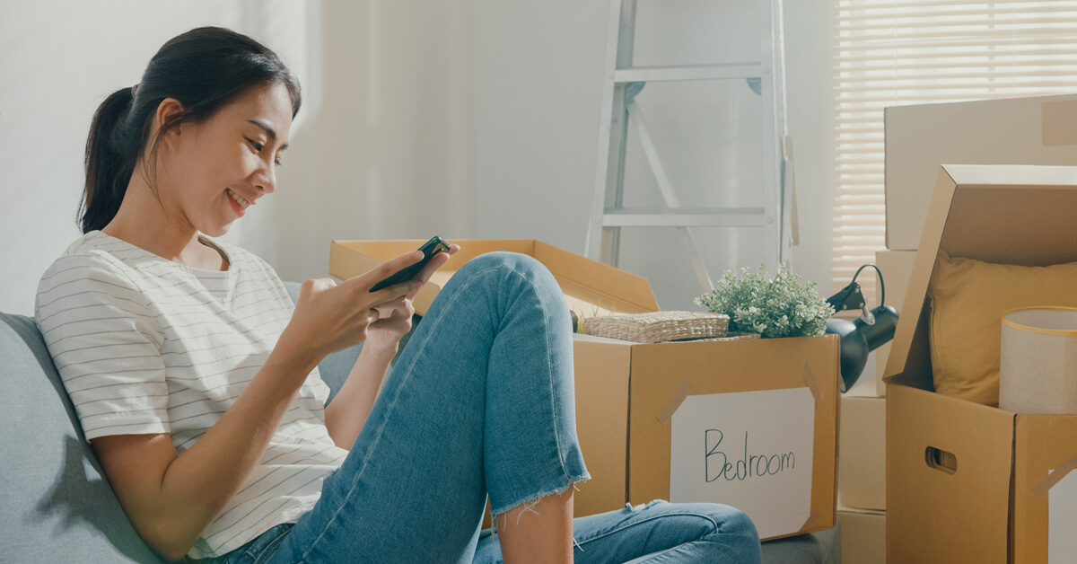 women using mobile banking app sitting in front of packed boxes