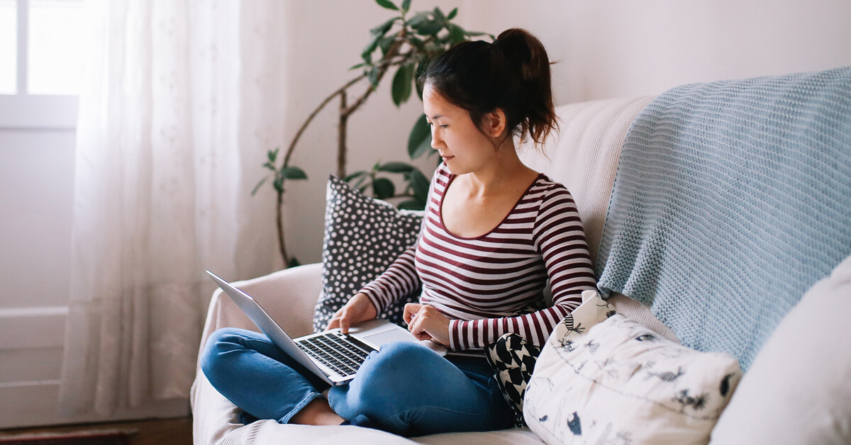 woman in striped shirt sitting on couch using a laptop